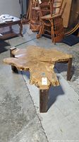 Live edge coffee table showing irregular shape, thick slab top and square wooden legs from an angle