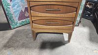 Front view of mid-century nightstand showing two drawer fronts with metal handles and wood grain finish.