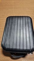 Closed hard-sided black front of carrying case on wood surface