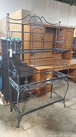 Full view of the black metal pie rack showing its open frame design and two glass shelves.