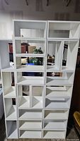 Front view of assembled white storage cubes forming a tall shelving unit with various rectangular compartments.