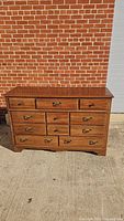 Front view of the dresser showing 11 drawers with brass handles and pulls, medium brown wood finish, and molding detail.