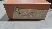 Original carrying case closed showing two-tone brown and beige textured exterior, plastic handle and metal latch.