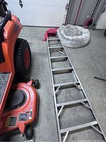 Full view of 10 ft aluminum ladder laid flat on concrete floor showing rungs, supporting braces and feet.