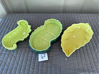 Three ceramic dishes shown from top view on gray surface, including leaf shapes in green and yellow and a kidney-shaped dark green dish.