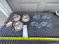 Photo showing three English ceramic cups and saucers with floral and gold trim, one extra matching cup, and four clear blue depression glass cups and saucers.