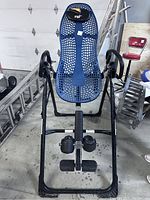 Front view of the black metal frame back stretcher showing the blue perforated plastic body support, ankle holders, and hand grips.