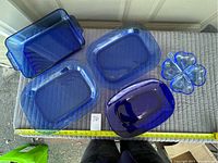 Four blue glass dishes on a quilted grey surface: three rectangular platters of different sizes and one clover-shaped divided dish, with measuring tape showing size reference.
