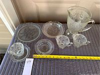 Overview of water pitcher, creamer, sugar bowl, and plates showing Iris floral depression glass pattern with measuring tape.
