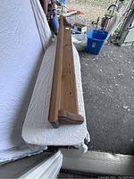 Top view of the entire pine shelf showing grain, thickness, and length placed on a mattress or cushion surface indoors near an open garage or door.