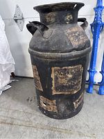 Milk can with vintage paper labels visible, showing its aged black metal body and dual handles.