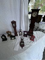 Full view of nine Franklin Mint miniature clocks arranged on white tablecloth, showing variety of styles and colors.