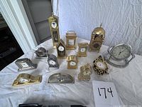 Overview of the 14 mini clocks laid out on a white cloth, showing different shapes and materials including brass and silver-tone finishes.