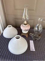 Full view of antique hand-painted oil lamp with clear glass chimney, brass base, two white glass shades, and lot tag.