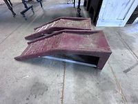 Side view of two red steel car ramps showing structural shape and wear.