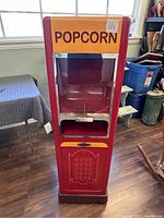 Front view showing clear popcorn compartment, large orange sign with 'POPCORN', metal latch and red body.