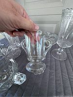 Close-up photo of a clear pressed glass spooner with scalloped top and two handles, held by hand to show size and details.
