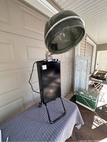 Front angled view of the retro portable salon hair dryer showing black hood, metal stand, and base on a moving blanket.