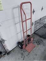 Full view of the red steel dolly showing the frame, handle, and the base plate on the floor.