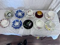 Photo showing all 10 teacups and saucers arranged on white cloth, highlighting variety of floral and decorative patterns