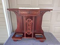 Front view of the walnut umbrella and cane stand showing the marble top, drawer, and carved central panel.