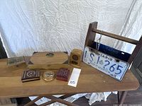 Photo showing all items in the lot arranged on a wooden table including the various trinket boxes and the wooden tool box with the license plate.