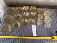 Full view of all 18 pieces including plates and dessert cups placed on quilted surface with measuring tape for size reference.