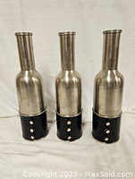 Photo of three silver and black decorative bottles or vases with metallic silver tops and black textured bases with studs.