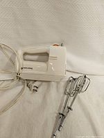 White Black and Decker hand mixer with two stainless steel beaters laid on a white fabric background.