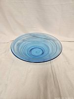 Top-down view of a blue spiral patterned glass bowl placed on a light cloth background, showing the full circular shape and spiral design.