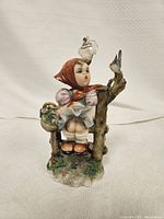 Front view of the Campodimante Bimba Piantina figurine showing the young girl sitting on a bench with a bird on a tree branch, detailed paint and colors visible.