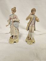 Front view of two porcelain figurines, depicting a woman holding a fan and a man in 18th-century clothing.