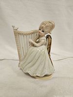 Front view of the porcelain girl figurine sitting on a chair playing a harp, glossy finish visible.