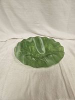 Green marbled scalloped plate resting on a white textured surface, showing full top view with scalloped edge detail and marbled color pattern.