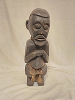 Front view of the large dark wooden carved statue showing detailed facial features and clasped hands.