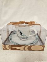 New Northwest Spirit tea cup and saucer set still sealed in original clear plastic packaging with brown ribbon, showing decorative black, purple, and blue colors.