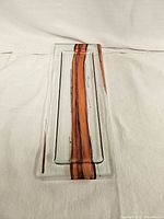 Clear rectangular decorative glass plate with a vertical red stripe in the center placed on a white textile background.