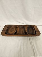 Photo showing wooden rectangular snack tray holding three smaller oval wooden bowls.