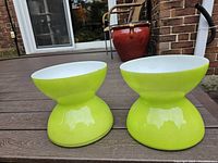 Two vivid lime green glass hourglass shaped vases on a wooden table, with a brick and patio background, showing color and shape clearly.