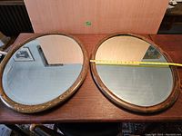 Photo showing both oval mirrors side by side on a wooden surface with a measuring tape indicating about 31 inches length.