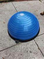 Side/top view of blue dome shaped Bosu balance half ball on black base on outdoor concrete ground.