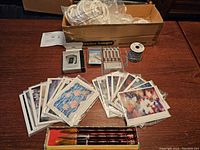 Full lot displayed with calligraphy brushes in box, art cards spread on table, pedometer box, chain roll, and closet hanging system box.