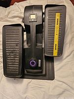 Full top view of Cubii under desk elliptical exercise machine showing wide foot pedals and central housing with LCD screen and resistance dial with ruler for scale.