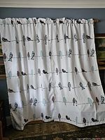 Two white curtains with bird print hanging on a curtain rod, showing design and length.