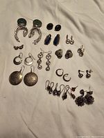 All earrings in lot laid out on white cloth showing mixed styles and materials including silver, natural stones, and glass.