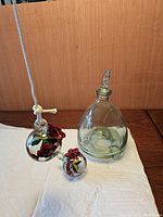 Full view of two glass hummingbird feeders and one clear glass wasp trap on white cloth.