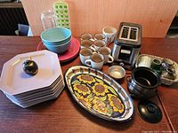 Overview of assorted kitchen items including plates, serving dish, small coffee cups, toaster and mini crock pot.