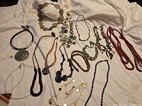 Full overview of the lot showing multiple necklaces and some bracelets with varied styles and materials laid on white fabric.