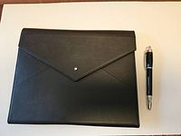 Black leather folio with flap closed, pen alongside for scale