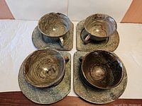 Top-down view of four raku pottery cups placed on matching saucers arranged in a square pattern on a white cloth surface.